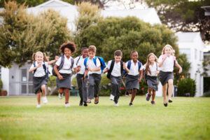 "Image of a diverse group of smiling school children running together in a classroom, engaged in learning activities and interacting with each other."